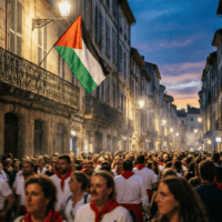 Foule en tenue blanche et rouge des fêtes basques sous un drapeau palestinien déployé au balcon